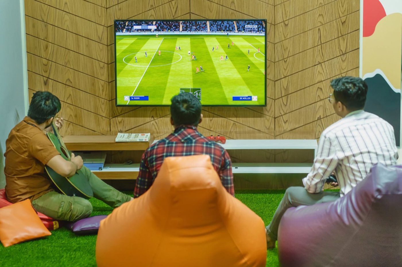 Three friends on bean bags watching a football match on a big screen