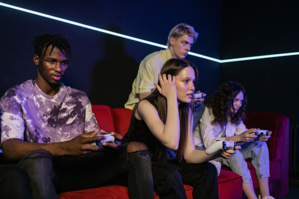 Four friends on a red sofa, controllers in hand, in a neon-lit room