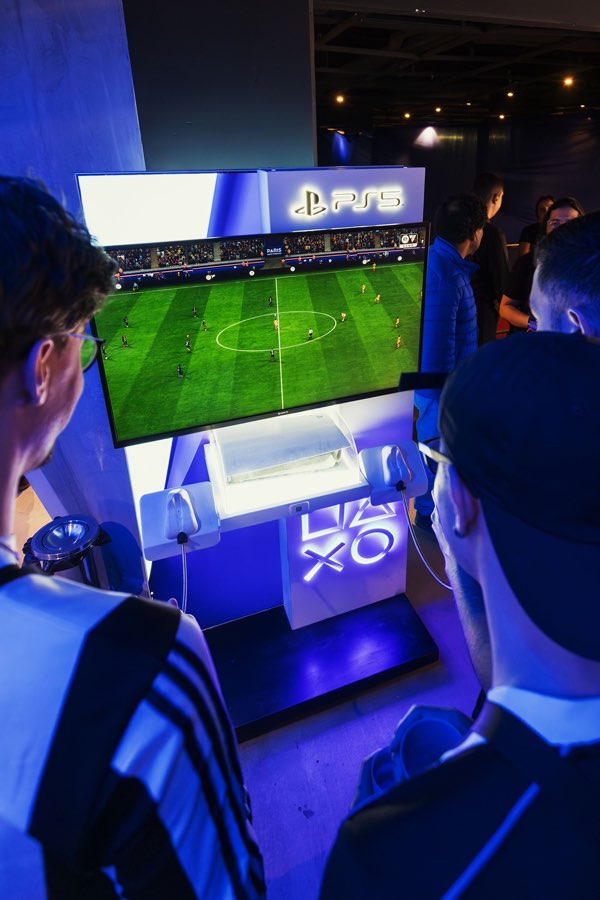 Players crowding around a PS5 screen showing a football match