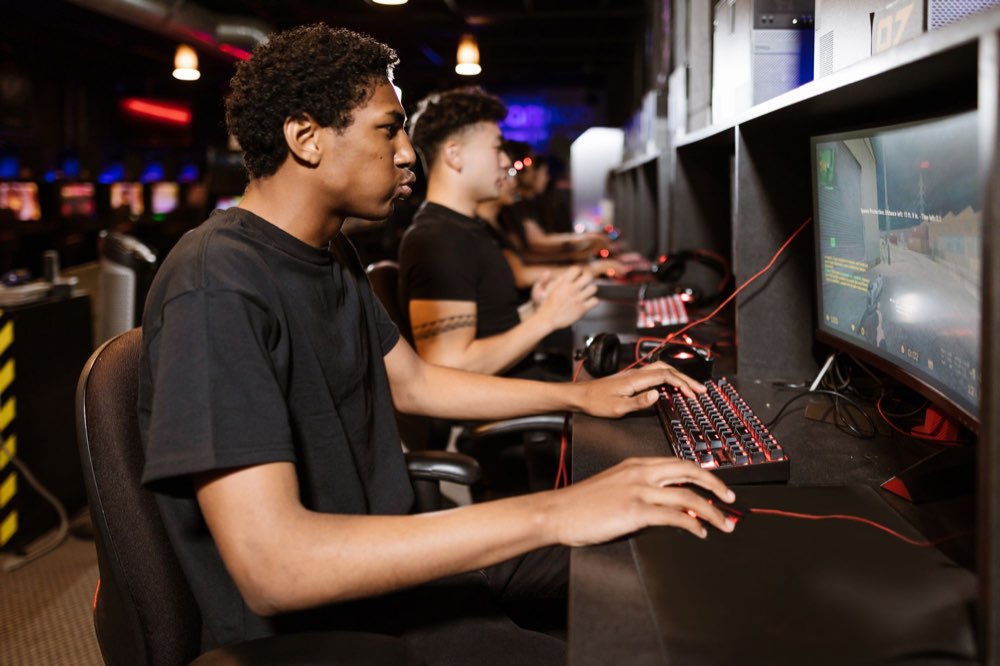 Row of players on gaming PCs with a shooter on screen