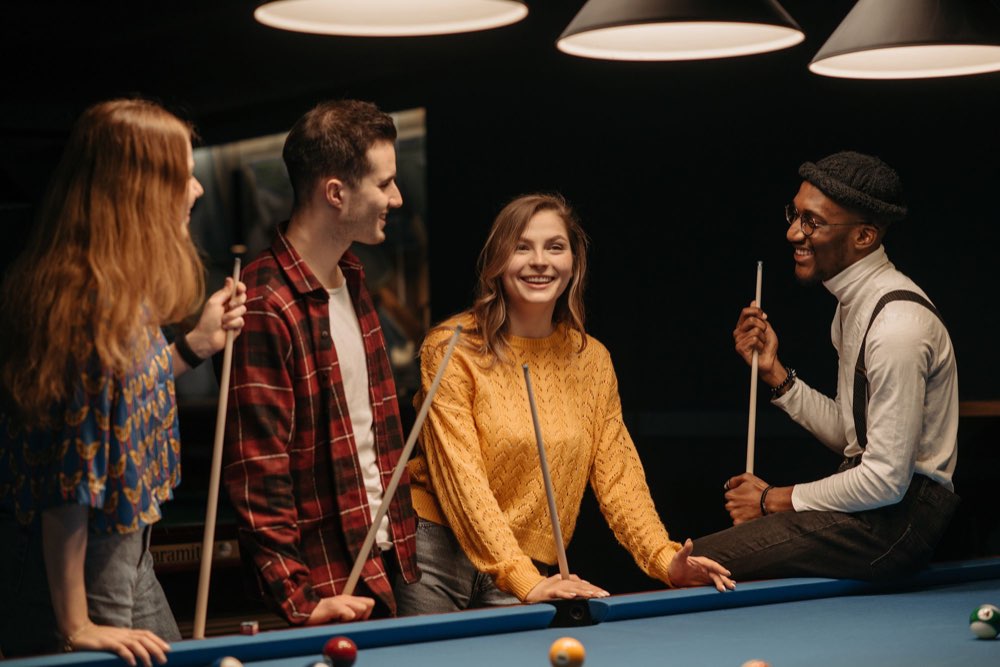 Friends laughing with cues around a pool table